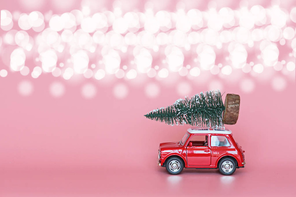 Красная игрушечная машина с рождественской ёлкой на крыше на розовом бумажном фоне. Зимняя доставка, поздравления с наступающим Новым 2020 годом. Открытки, макет
 - Фото, изображение