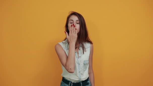 Pretty caucasian young woman blowing kiss over orange wall - Felvétel, videó