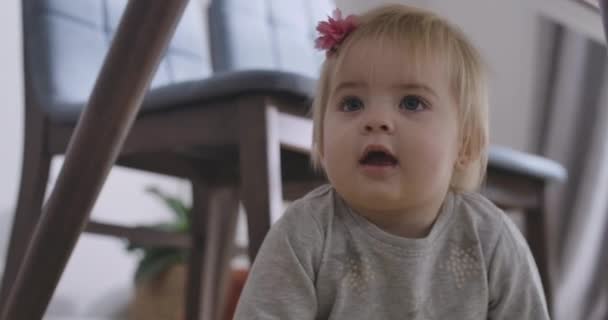 Portrait of charming Caucasian baby girl with grey eyes and blond hair looking away with open mouth. Portrait of charming child hiding under the table. Cinema 4k ProRes HQ. - Кадры, видео