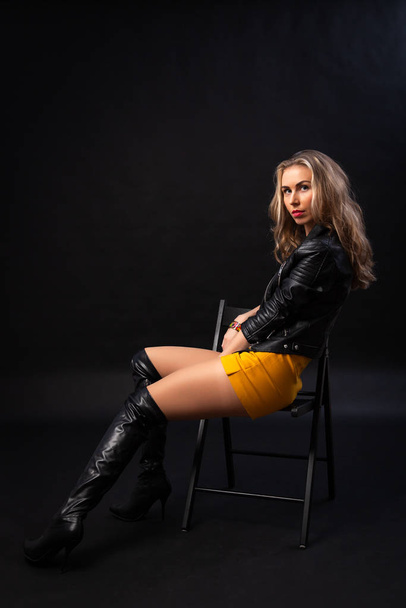 Concept attractive bitch woman. Beautiful woman in fashionable clothes in yellow skirt, black lether coat and attractive bitch posing in a studio shot. Portrait of a modern successful woman - Valokuva, kuva