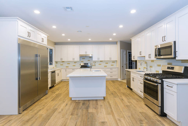 Keittiö, jossa on saaren pesuallas kaapit, ja parkettilattia uudessa ylellisessä kodissa kolme keittiön pesuallasta
 - Valokuva, kuva