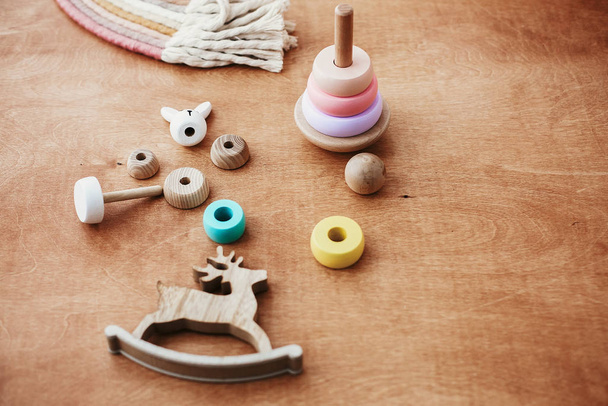 Stylowe drewniane zabawki dla dzieci na drewnianym stole. Nowoczesna, kolorowa drewniana piramida z rozbieranymi pierścieniami i tęczą makramy. Ekologiczne, plastikowe zabawki edukacyjne dla malucha - Zdjęcie, obraz