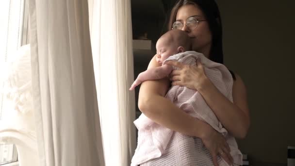 jonge moeder wiegt haar kind door het raam en glimlacht - Video