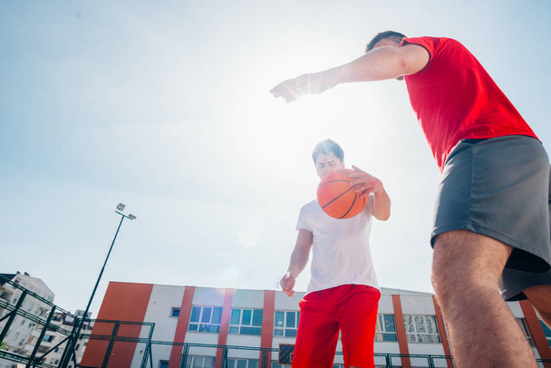 晴れた日にバスケットボールコートでボールを所持するために戦う2人の白人バスケットボール選手. - 写真・画像