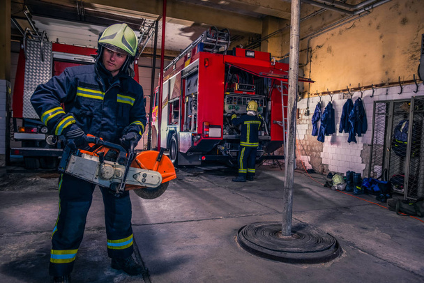 Un pompier avec uniforme et casque tenant une scie à chaîne avec feu t - Photo, image