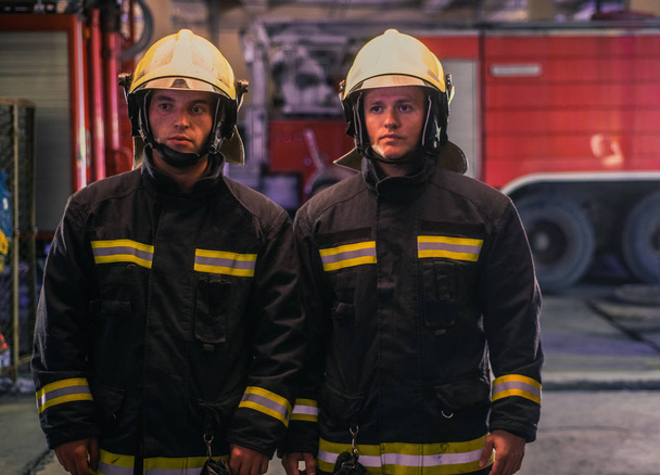 Portrait of two young firemen in uniform standing inside the fir - Fotó, kép