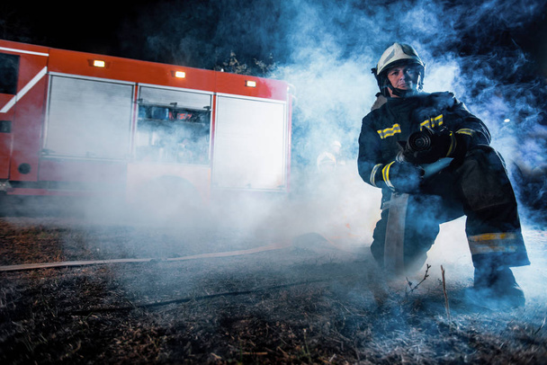 Une équipe de pompiers en train de faire fonctionner un tuyau d'arrosage dans un endroit rempli de fumée - Photo, image