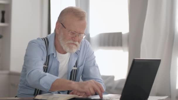 modern age, attractive pensioner with gray beard in glasses pays utility bills online working at computer - 映像、動画