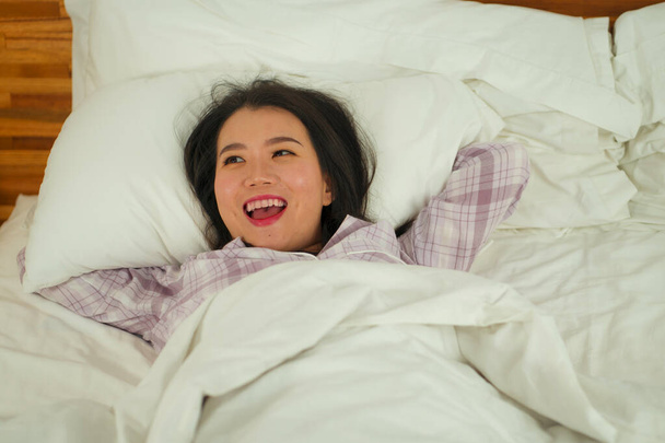 lifestyle portrait of young beautiful and sweet Asian Korean woman in bed feeling happy and relaxed wearing cute pajamas enjoying lazy Sunday morning at home  - Photo, image