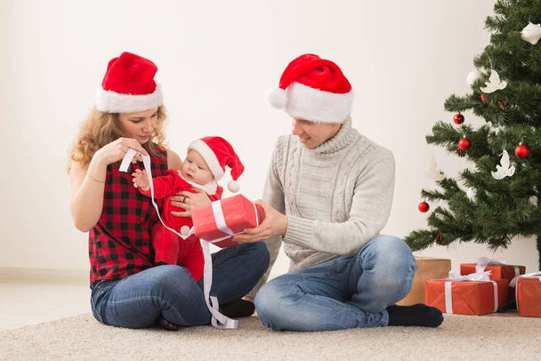 Holidays, children and family concept - Happy couple with baby celebrating Christmas together at home. - Фото, изображение