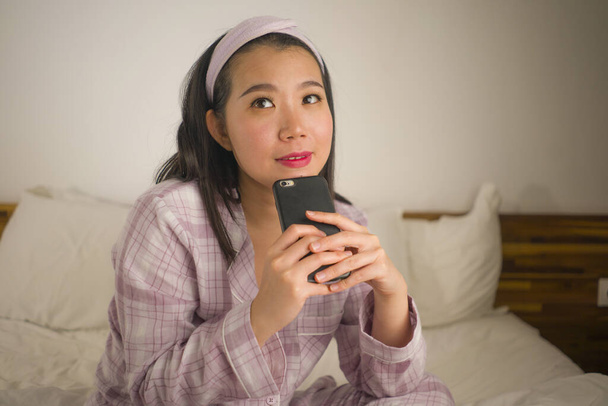 young beautiful and sweet Asian Chinese woman in cute pajamas  playful in bed using mobile phone enjoying social media or online dating app happy and relaxed  - Foto, Imagen