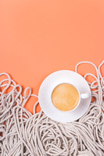 Minimalistic cotton white rope background with cup of cappuccino on a coral colored background. - Photo, Image