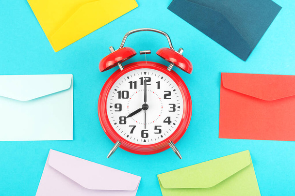 Colorful envelopes around the red alarm clock on a blue background - Фото, изображение