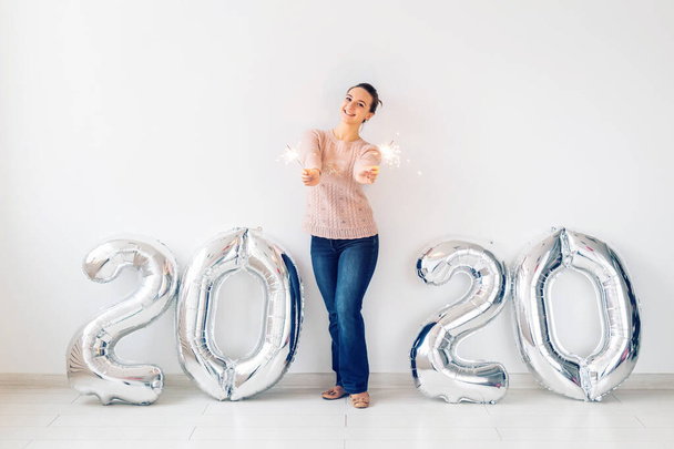 New Year celebration and party concept - Happy young woman with sparklers near silver 2020 balloons on white background. - Foto, imagen