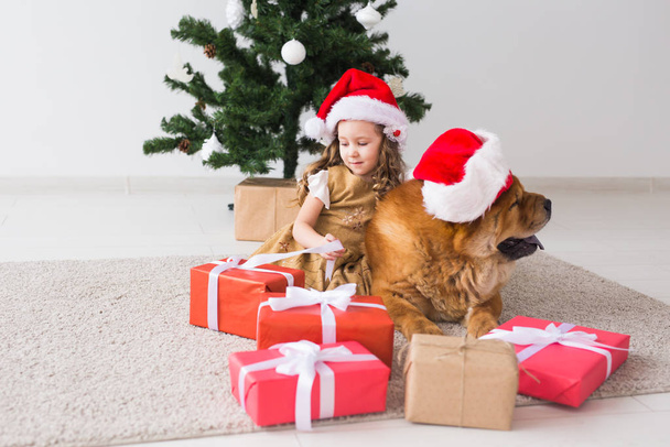 Concept enfants et animaux de compagnie - Jolie fille avec chien de bouffe assis près du sapin de Noël. Joyeux Noël et Joyeuses Fêtes
. - Photo, image
