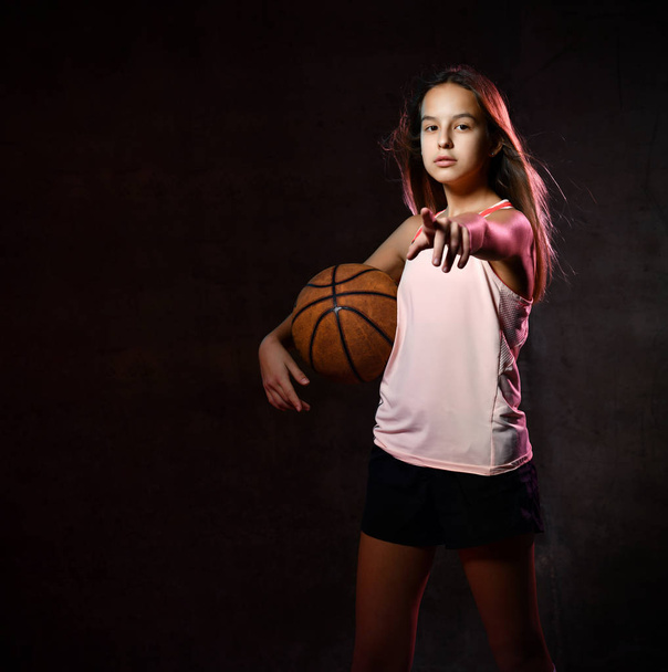 Beautiful caucasian teen woman in sportswear playing basketball . Sport concept isolated on black background. - Fotó, kép