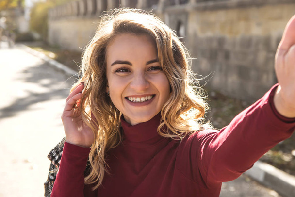 Hermosa chica caucásica toma una selfie en la ciudad de otoño y sonríe
. - Foto, Imagen