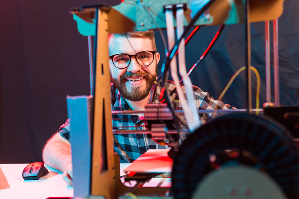 Fiatal férfi tervező mérnök, aki 3D nyomtatót használ a laboratóriumban, és tanulmányozza a termék prototípusát, technológiáját és innovációs koncepcióját - Fotó, kép