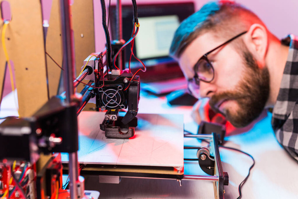 Concept de technologie et d'ingénierie - Ingénieur masculin travaillant la nuit en laboratoire, il ajuste les composants d'une imprimante 3D
. - Photo, image