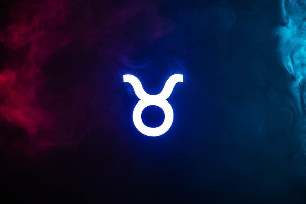 голубой подсвеченный знак зодиака Телец с разноцветным дымом на заднем плане
 - Фото, изображение