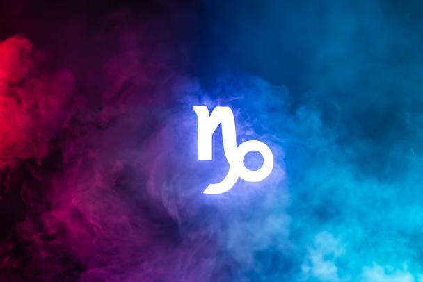 голубой освещенный знак зодиака Козерога с разноцветным дымом на заднем плане
 - Фото, изображение