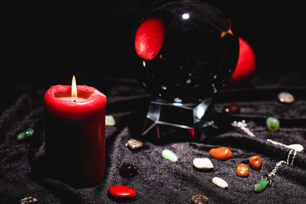 selectieve focus van kristallen bol met waarzeggerij stenen en kaars op zwart fluwelen doek - Foto, afbeelding