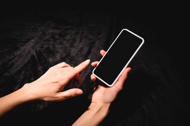 cropped view of woman holding smartphone with blank screen on black velvet cloth - Foto, afbeelding