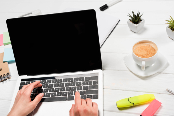 обрезанный вид женщины с помощью ноутбука на рабочем месте с офисными принадлежностями и кофе
 - Фото, изображение