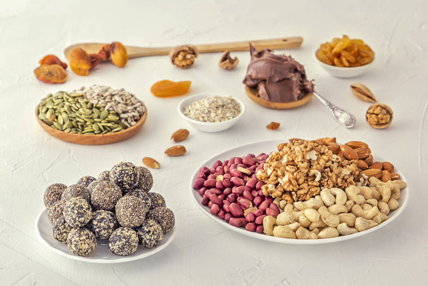 Mordidas naturais de energia bruta saudáveis, pasta de chocolate e mistura de frutas secas com nozes em uma mesa branca
 - Foto, Imagem