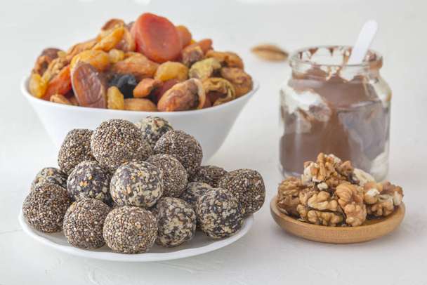 Mordidas naturais de energia bruta saudáveis, pasta de chocolate e mistura de frutas secas com nozes em uma mesa branca. Close-up
 - Foto, Imagem