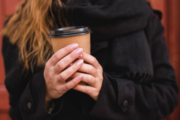コーヒーの紙コップを手に女性の手を取る。赤い壁にカップを持っている女性。晴れた日の午後. - 写真・画像