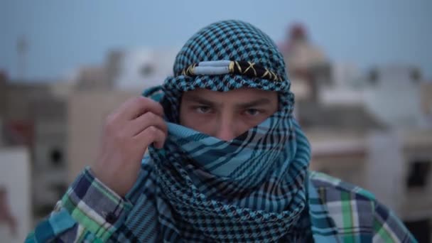 Nuori mies arabian nenäliinassa. Mies katsoo kameraan ja avaa nenäliinan. Talon katolla arabitalojen taustalla. - Materiaali, video