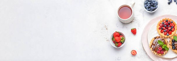 Sweet tartlets, berries and tea on light background  with space for text - Фото, изображение