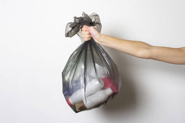 Main féminine tient un sac poubelle avec des ordures sur un fond clair. Concept de poubelle séparé, arrêter le plastique
 - Photo, image