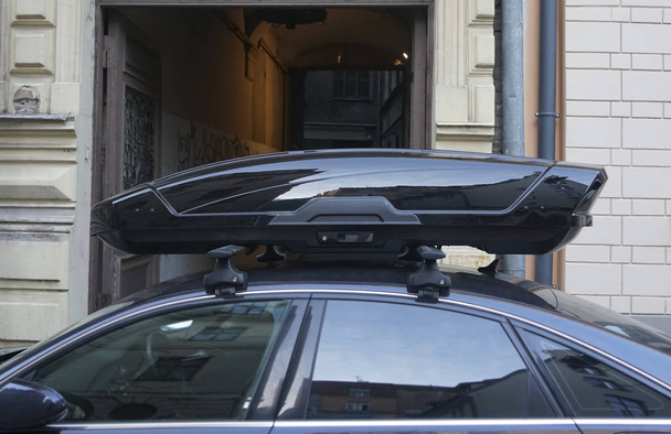 duży czarny bagażnik skrzynki na dachu ciemnego nowoczesnego samochodu. Podróże i akcesoria do transportu. skrzynka bagażnika zamocowana na dachu samochodu - Zdjęcie, obraz