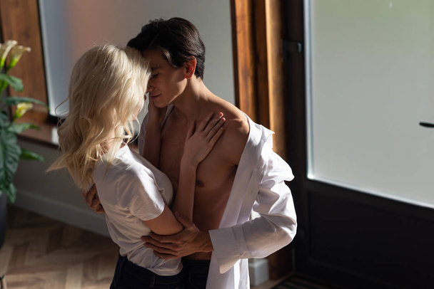 Blonde woman hugging shirtless man in living room - Foto, Imagem