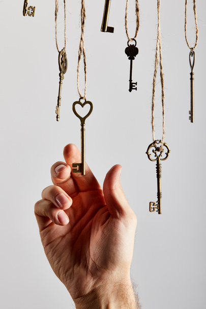 cropped view of man touching vintage keys hanging on ropes isolated on white - Zdjęcie, obraz
