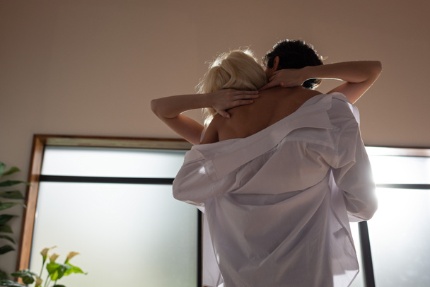 Back view of shirtless man embracing blonde woman in living room - Foto, afbeelding