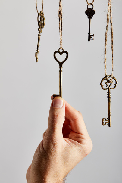 vista ritagliata di uomo toccare chiavi vintage appeso su corde isolate su bianco
 - Foto, immagini