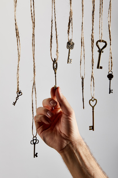 cropped view of man touching vintage keys hanging on ropes isolated on white - Foto, Imagen
