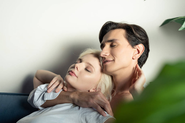 Side view of smiling couple with closed eyes embracing at home - Foto, Bild