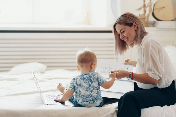 moderne Frau, die mit Kind arbeitet. Multitasking, Freiberuflichkeit und Mutterschaftskonzept - Foto, Bild