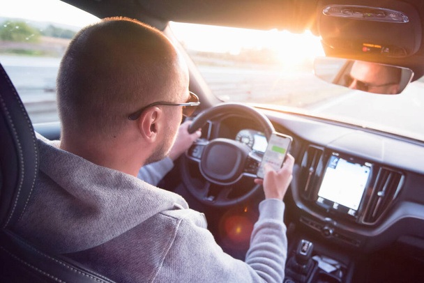 Человек смотрит на мобильный телефон во время вождения автомобиля. - Фото, изображение