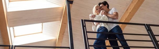 Panoramic shot of young couple with coffee embracing at balcony - Foto, Imagen