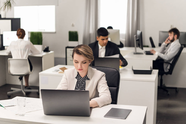 Woman work on laptop, men behind her looks through documents in office - Photo, Image