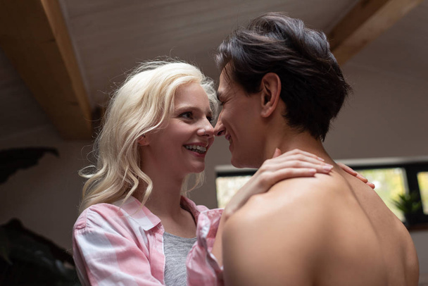 Smiling woman looking at shirtless boyfriend at home - Фото, изображение