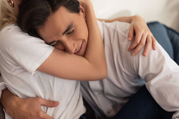 Sorrindo homem abraçando namorada no sofá na sala de estar
 - Foto, Imagem