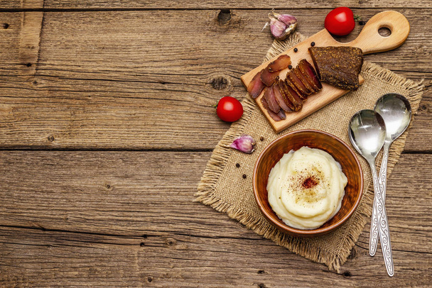 Homemade Thanksgiving garlic mashed potatoes with fresh tomatoes and pastrami. Sackcloth napkin, spoons, old wooden boards background - Photo, Image