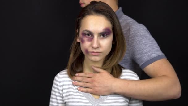 Egy fiatalember megölel egy fiatal nőt. Egy nő zúzódásokkal az arcán. Veszekedés egy fiatal családban. Családi erőszak. Fekete alapon - Felvétel, videó