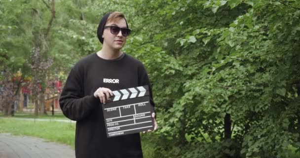 Young man with clapperboard in sunglasses outdoors. - Filmagem, Vídeo